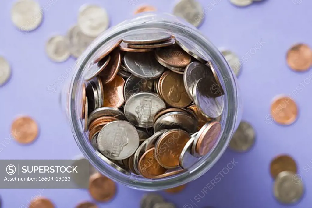 Glass jar with coins and scattered coins