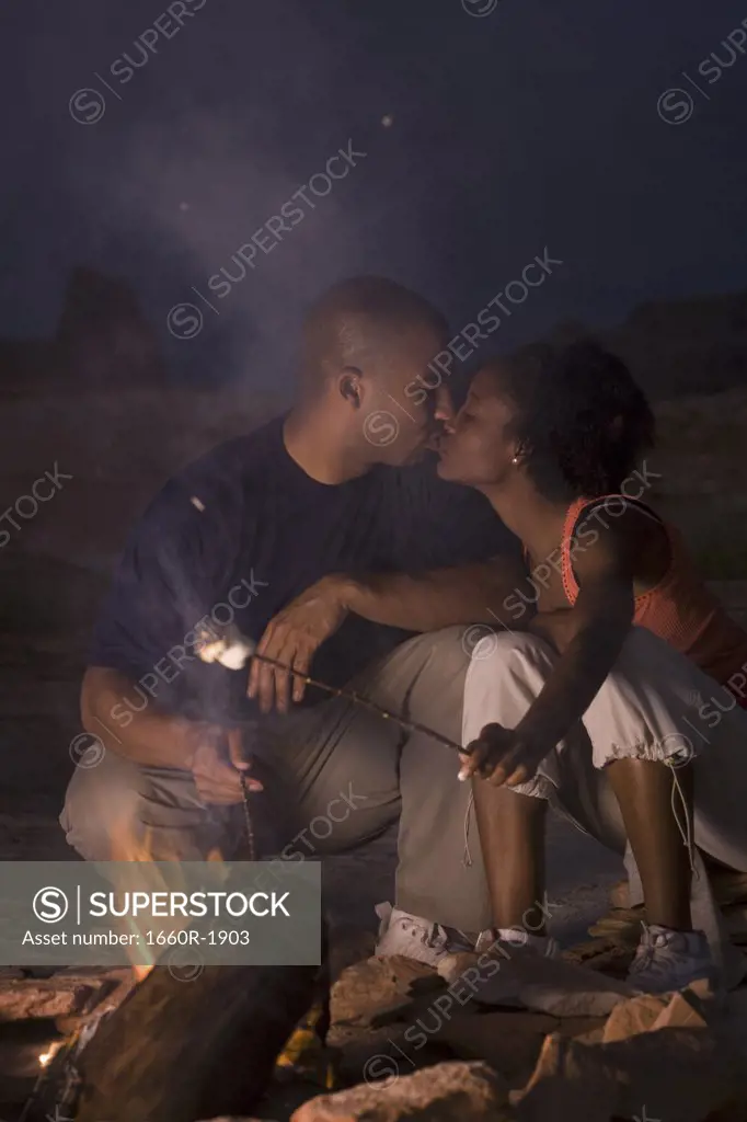 Young couple kissing by a campfire