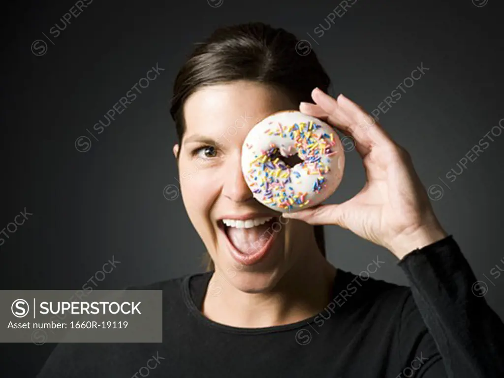 Woman holding donut up to eye and smiling