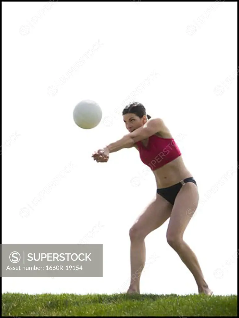 Woman in bikini playing volleyball outdoors on grass