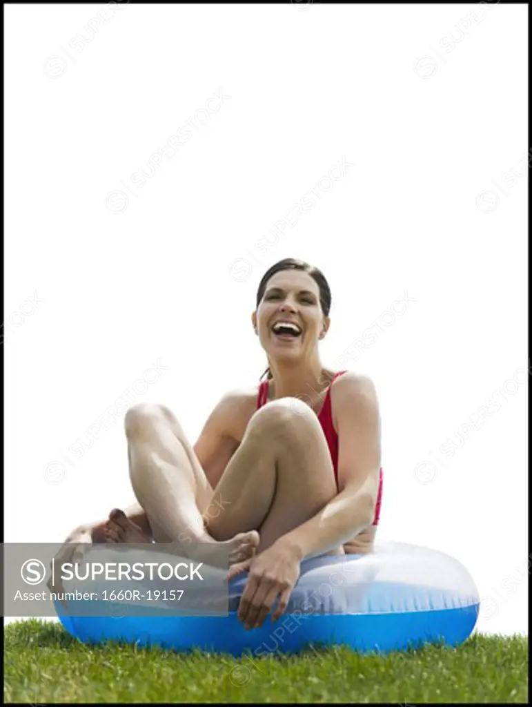 Woman sitting cross legged in swimming ring on grass laughing
