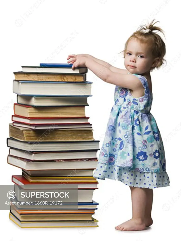 Young girl standing beside pile of hardcover books