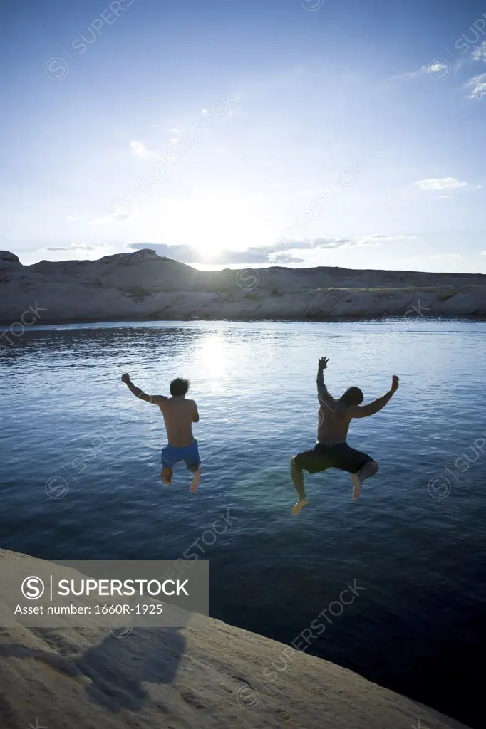 Rear view of two men jumping into a lake