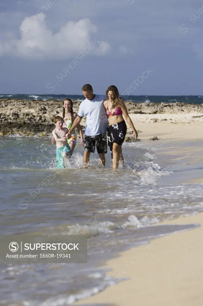 Couple with boy and girl walking in water on sandy beach