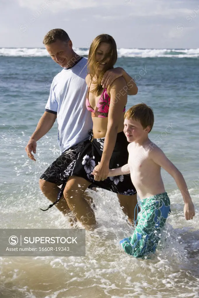 Couple with young boy walking in water on beach