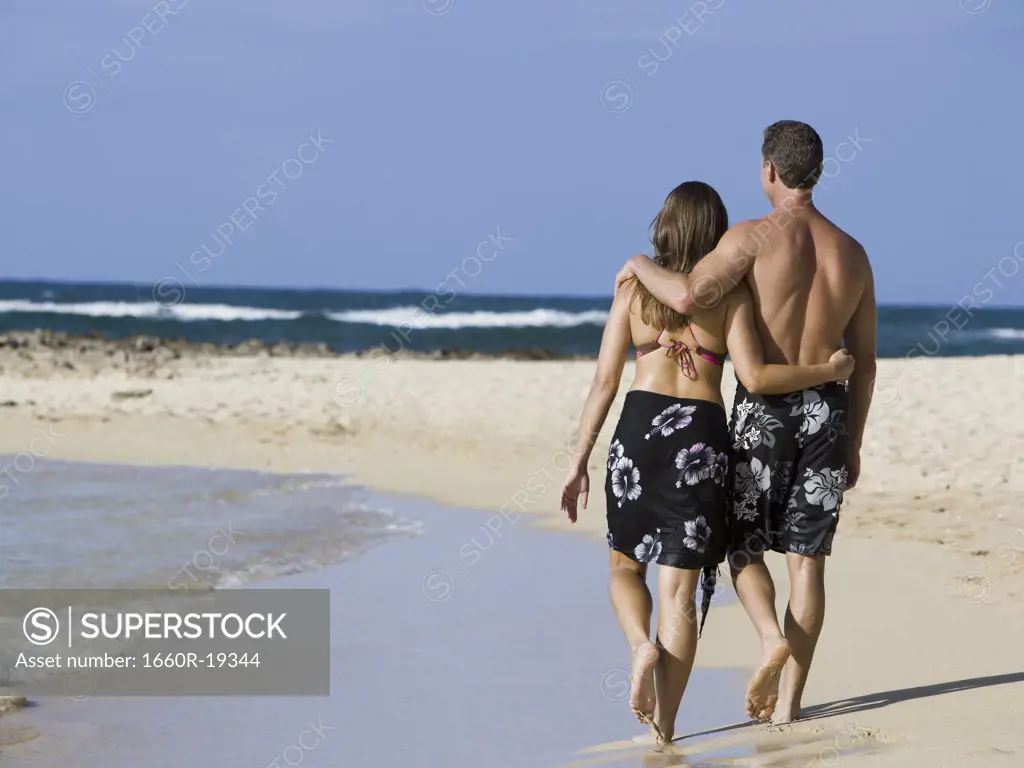 Rear view of couple walking on beach embracing