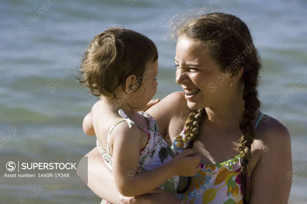 Teenage girl with braces holding baby girl outdoors smiling
