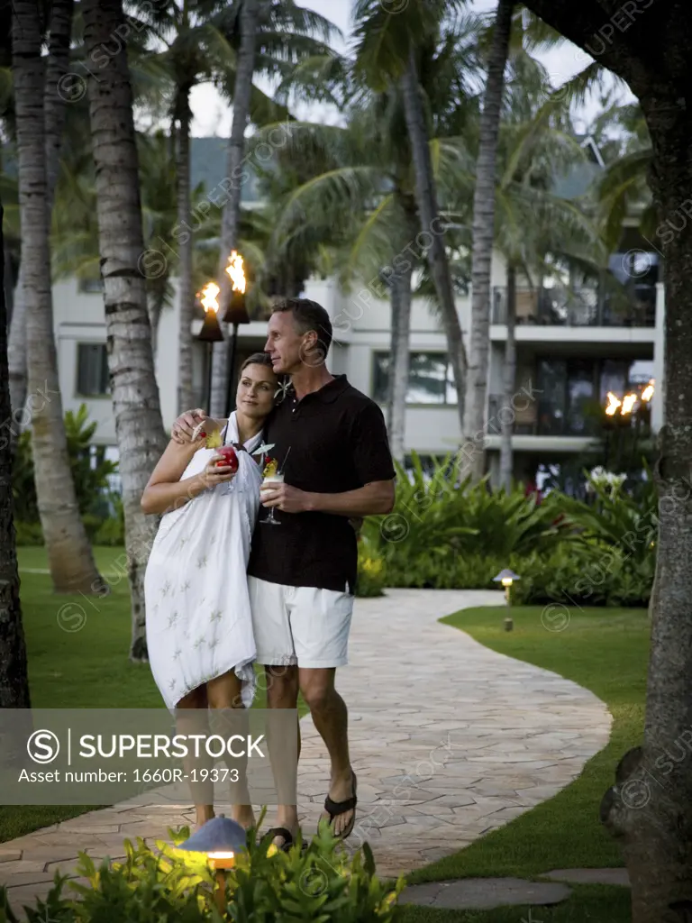 Couple with tropical cocktails walking at resort