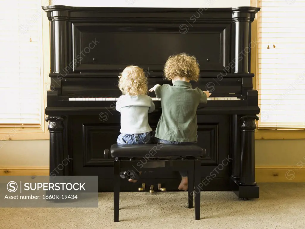 Rear view of two children sitting at upright piano