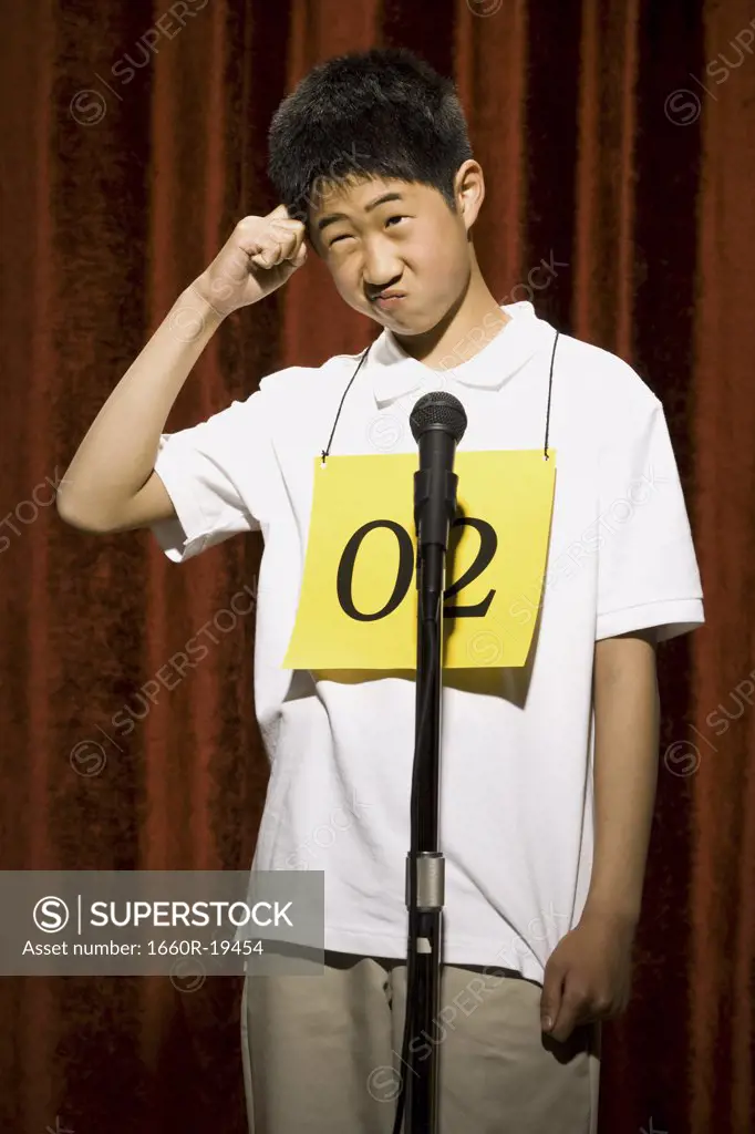 Boy at microphone with number around neck scratching head