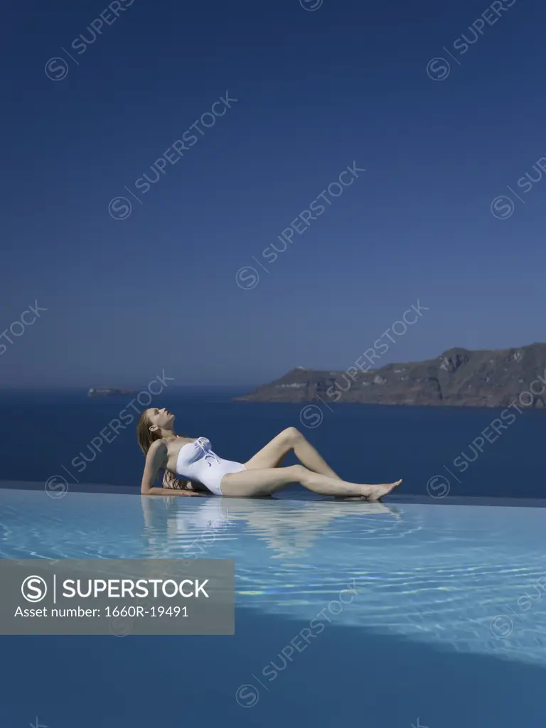 Woman in swimsuit reclining by infinity pool outdoors