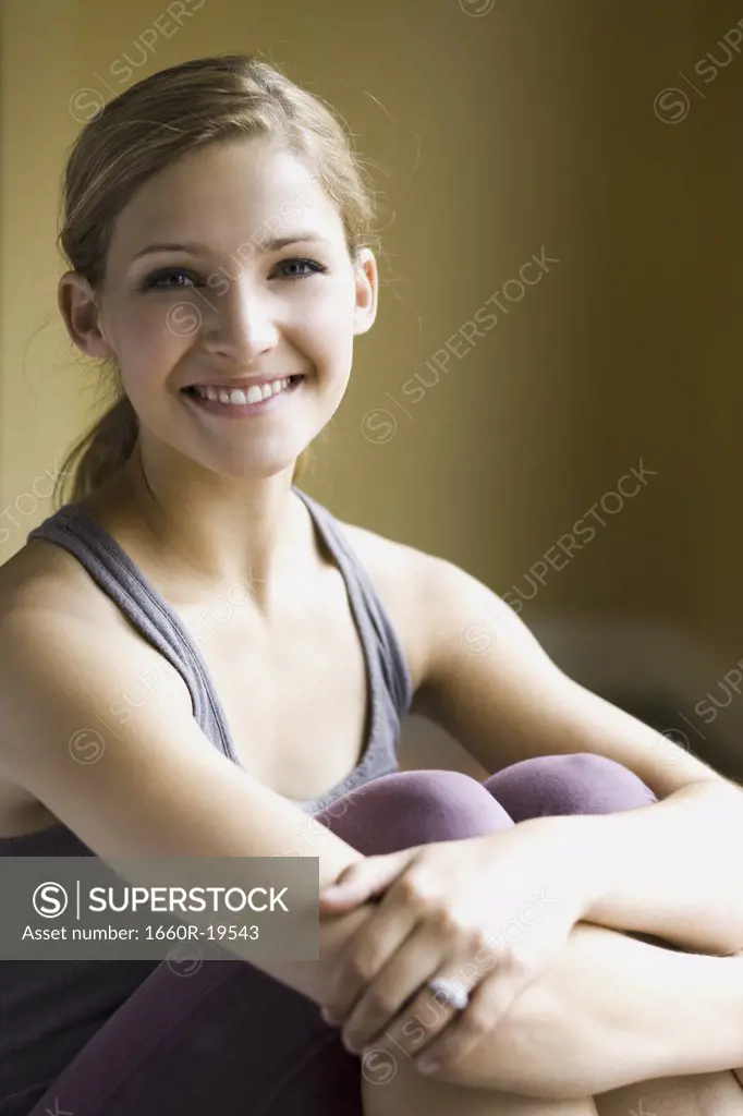 Woman sitting and smiling with arms around knees