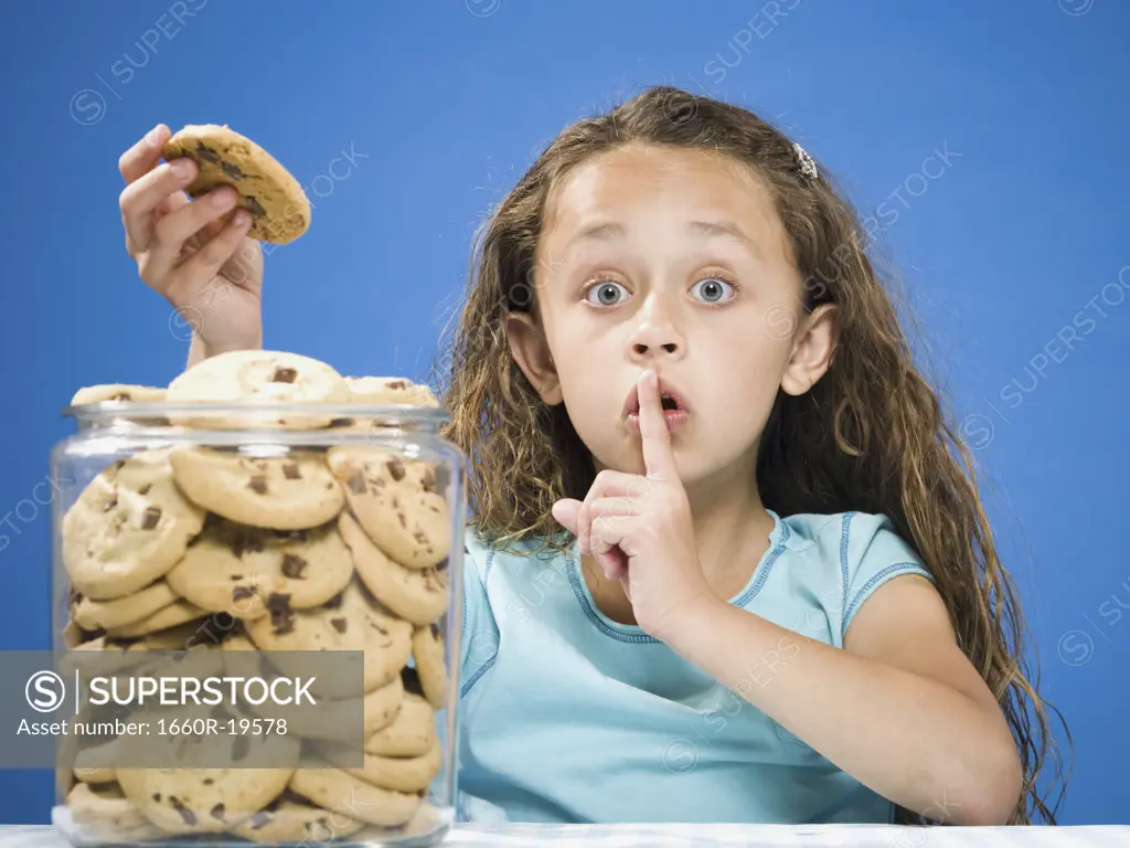 Girl taking chocolate chip cookie from jar and hushing