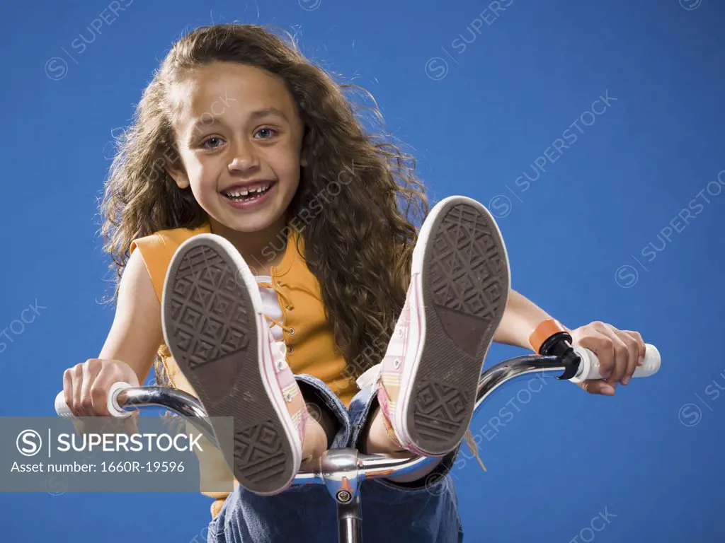 Girl riding bicycle with feet on handlebars