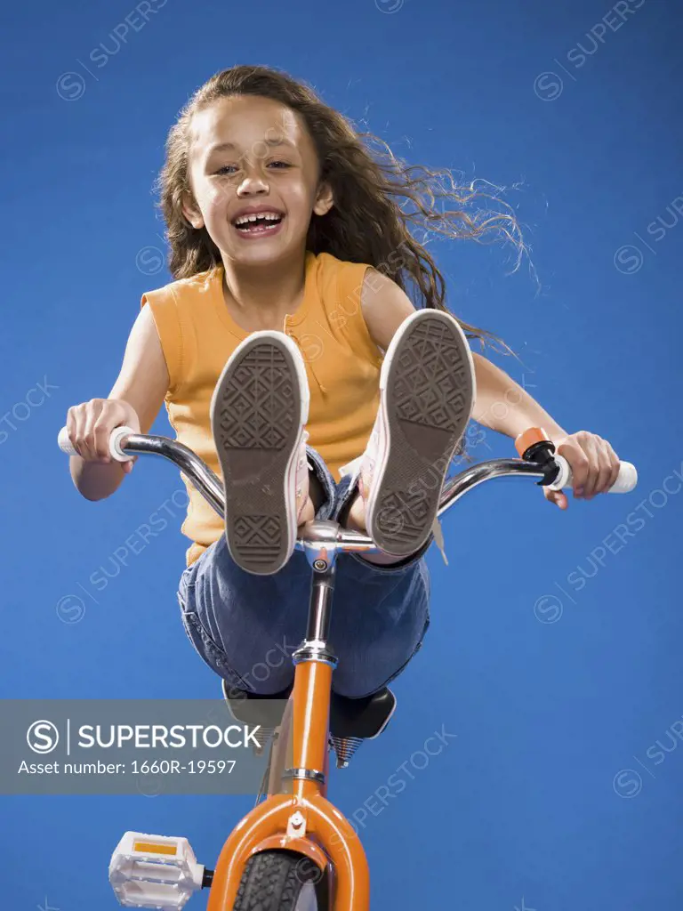 Girl riding orange bicycle with feet on handlebars smiling