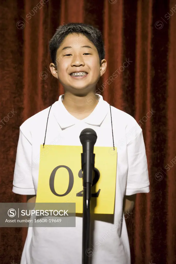 Boy contestant standing at microphone smiling with braces