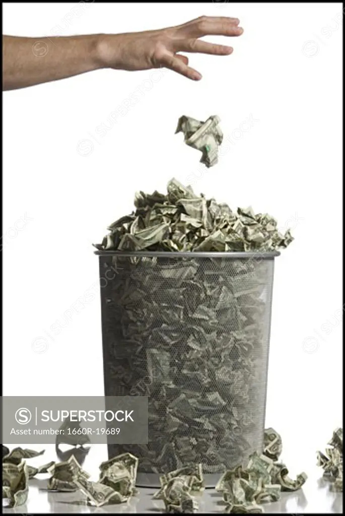 Person throwing crumpled money into waste paper basket
