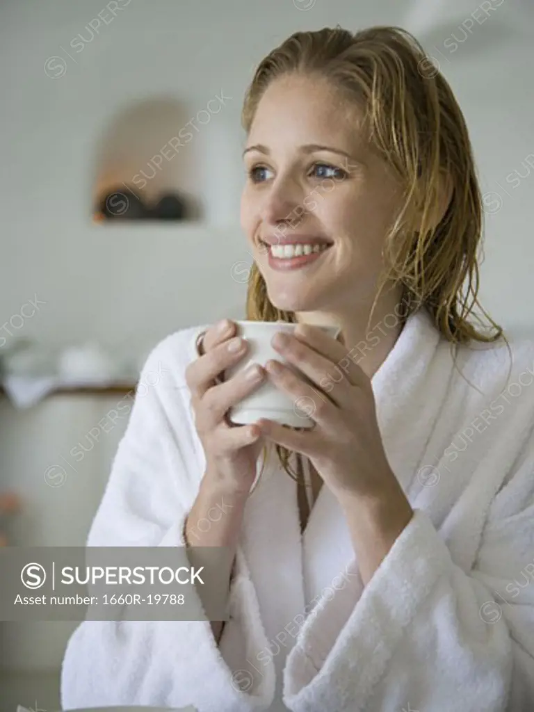 Woman in bathrobe holding mug smiling
