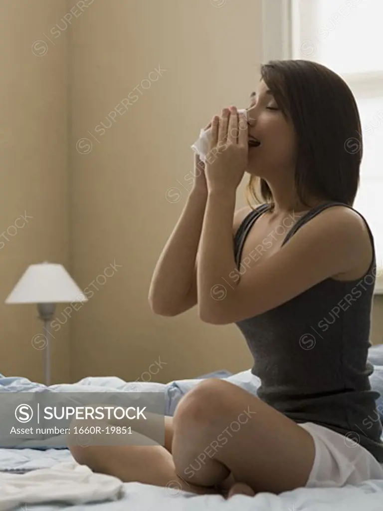 Woman sitting cross legged on bed blowing nose