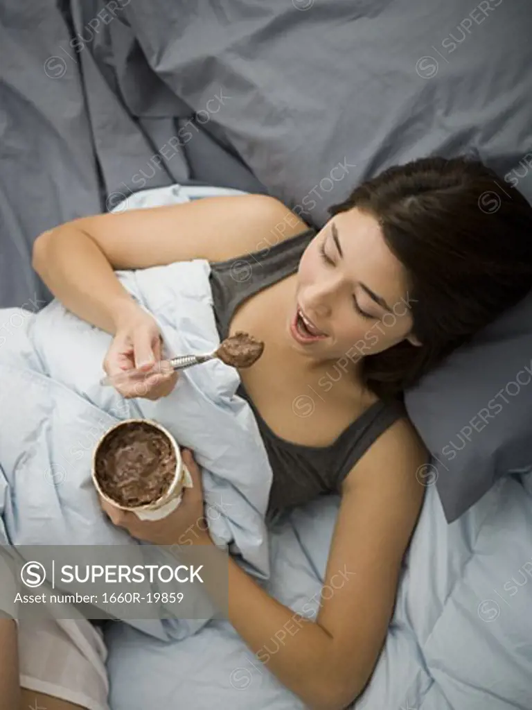 Woman lying in bed eating chocolate ice cream