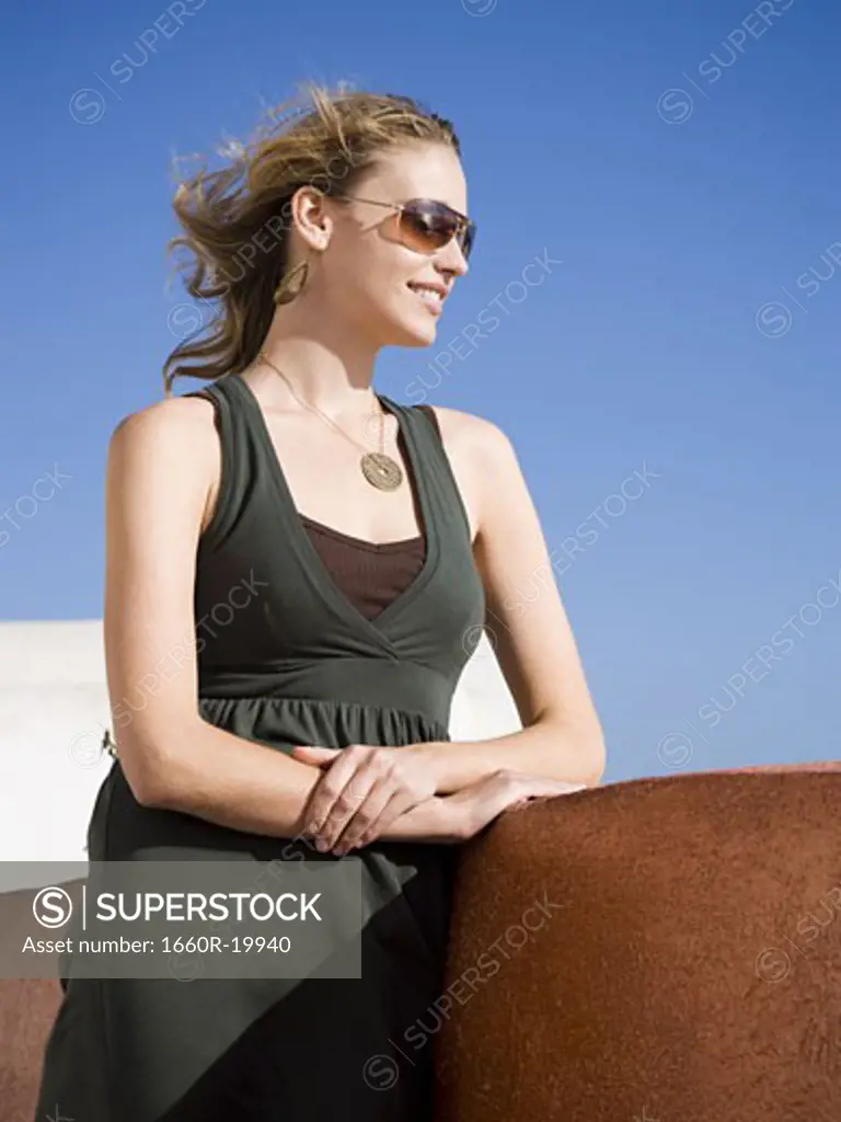 Woman in sunglasses outdoors leaning on wall smiling