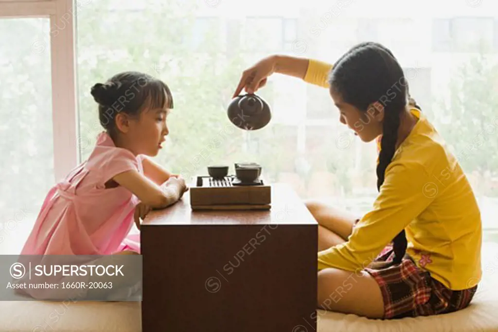 Profile of two girls sitting cross legged having tea