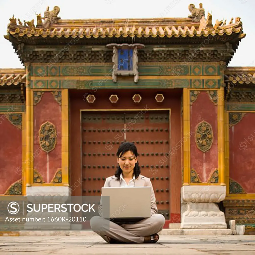 Businesswoman sitting cross legged outdoors with laptop