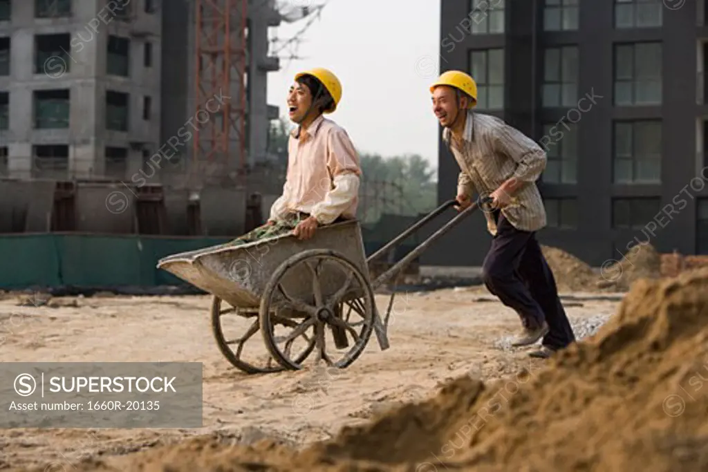 Construction worker giving other worker ride in wheelbarrow