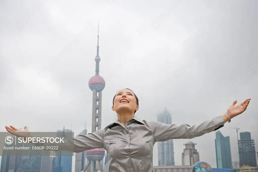 Businesswoman smiling outdoors with arms up and city skyline in background