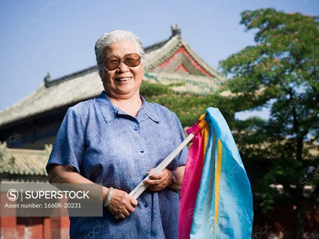 Woman standing outdoors with fabric on sticks with pagoda in background smiling