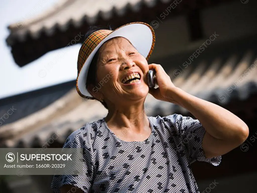 Woman with sun visor outdoors smiling talking on cell phone