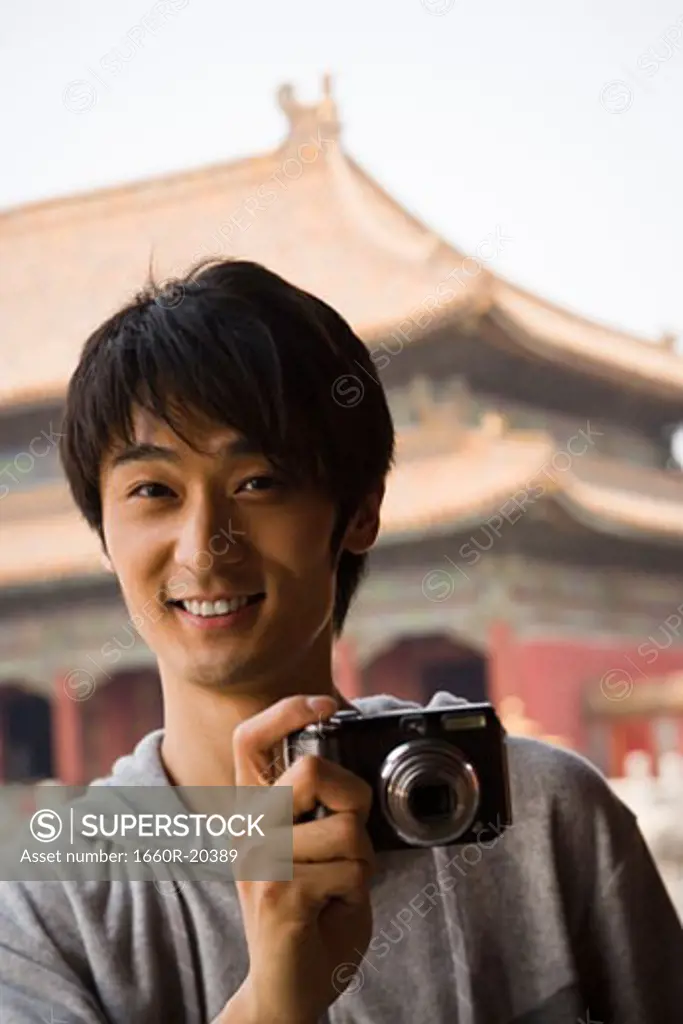 Teenage boy outdoors with digital camera smiling