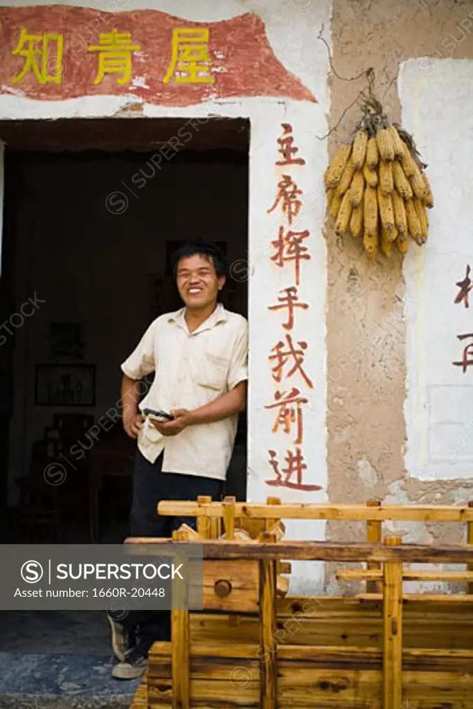 Man leaning on door frame with Chinese characters and corn hanging