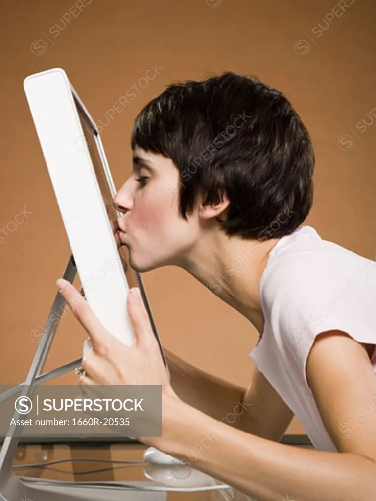 Profile of woman kissing computer monitor