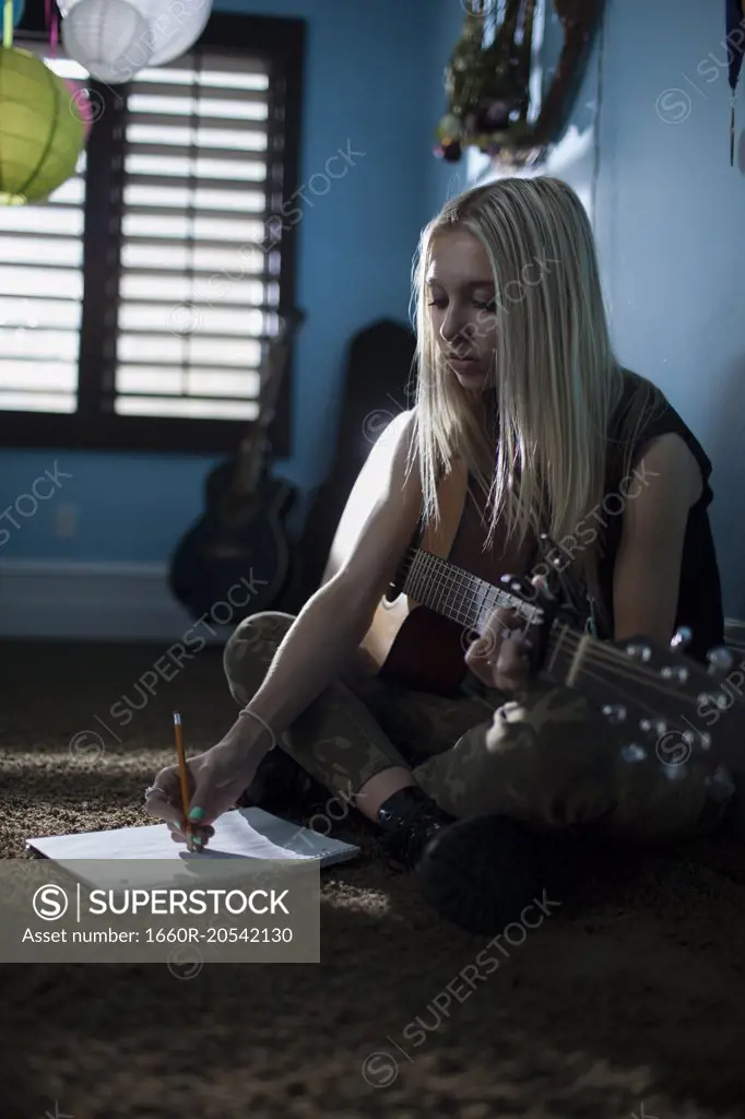 Concentrating musician writing music with acoustic guitar sitting cross legged on floor