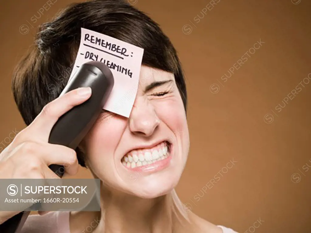 Woman stapling list of things to remember to her forehead and wincing