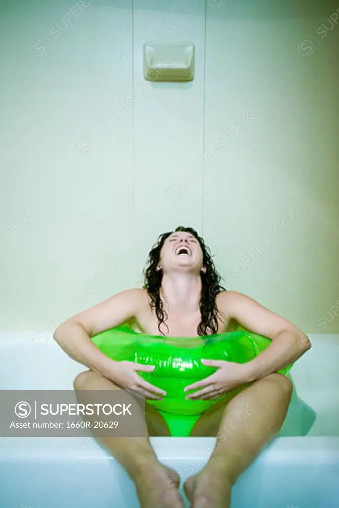 Woman sitting in bathtub with inflatable ring screaming