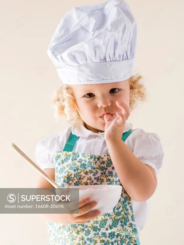 Little girl wearing a chef's hat and holding a bowl.
