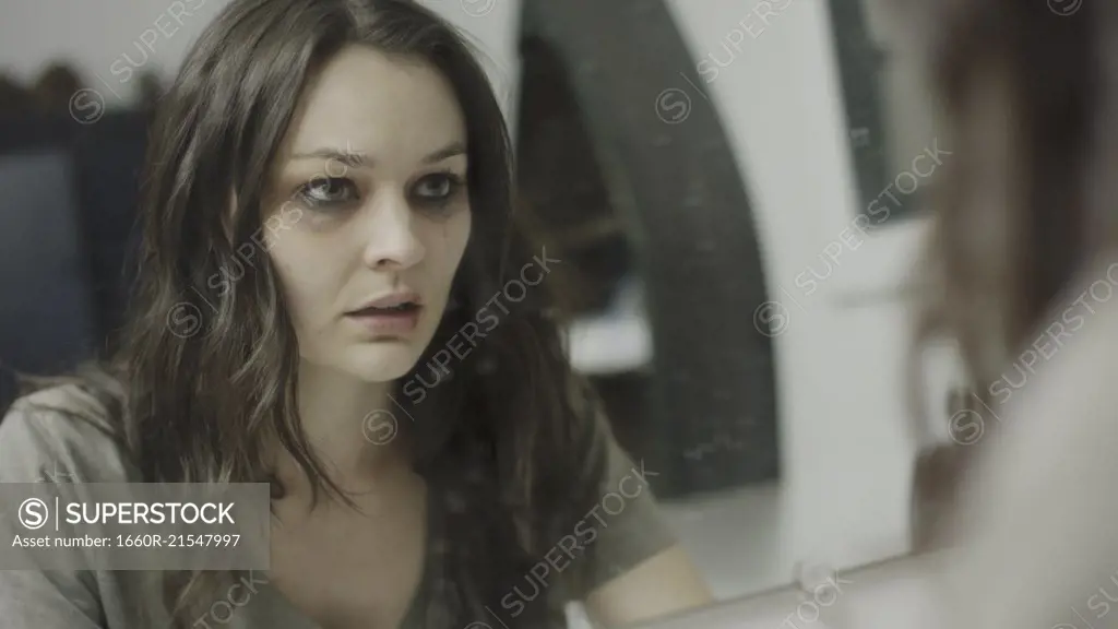 Selective focus view of sad battered woman examining her injured face in mirror