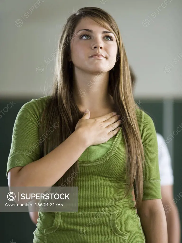 Young woman in a classroom with hand over heart.