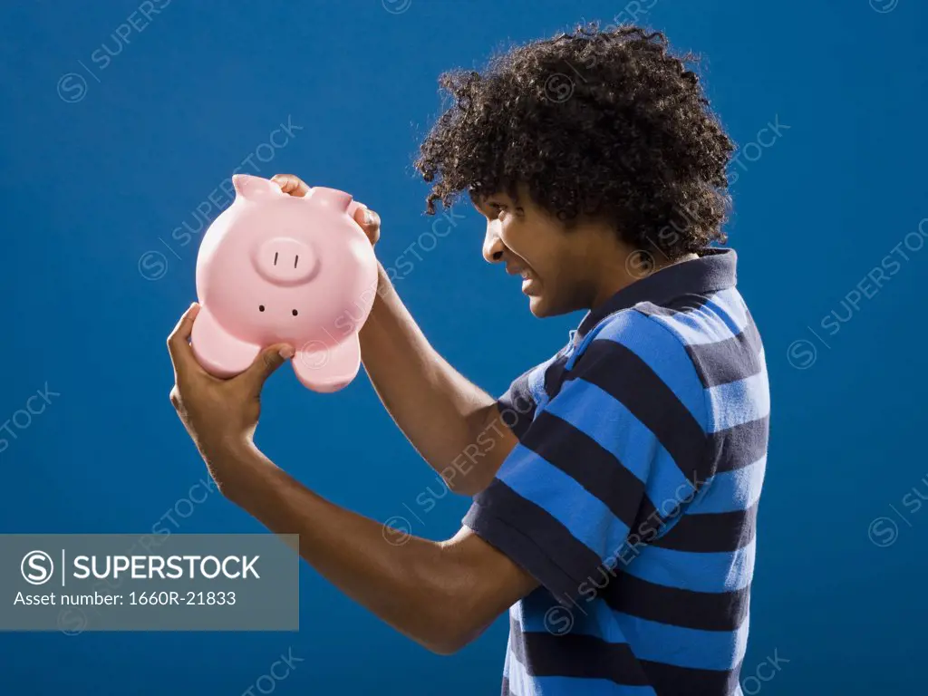 young man trying to get money out of a piggy bank.