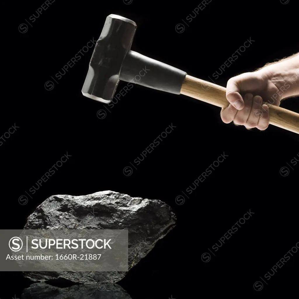 Hand swinging a sledge hammer toward a piece of coal.
