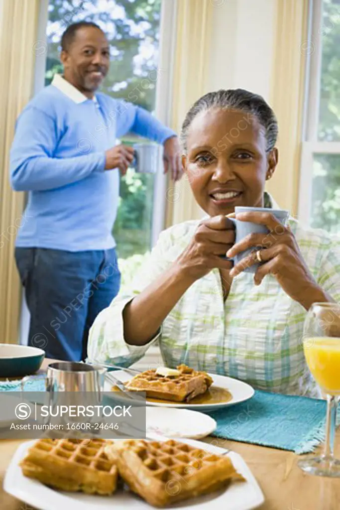 Portrait of a senior woman sitting at the breakfast table with a senior man standing behind her