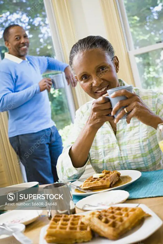 Portrait of a senior woman sitting at the breakfast table with a senior man standing behind her