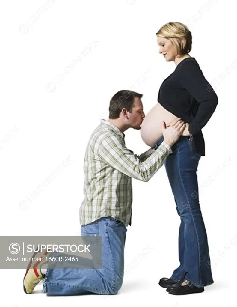 Side profile of a mid adult man kissing his pregnant wife's abdomen