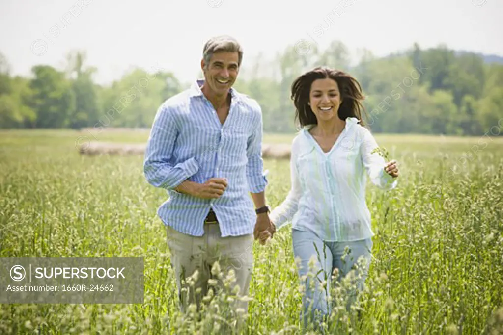Mature man and a mid adult woman holding hands and running in a field