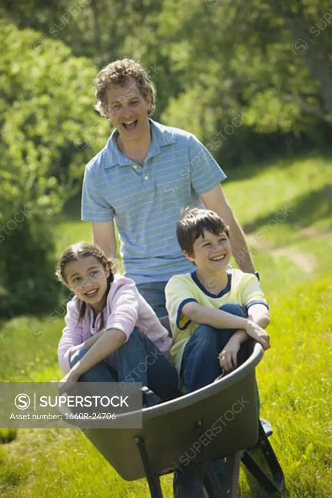 Man pushing his son and daughter in a wheelbarrow