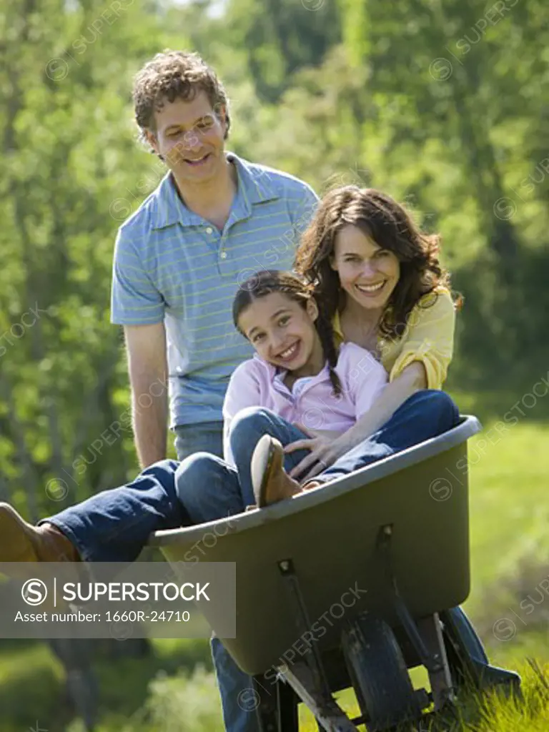 Man pushing his daughter and his wife in a wheelbarrow