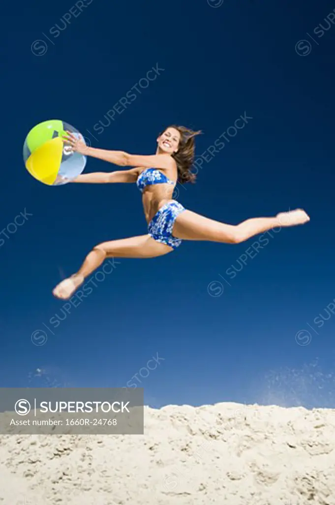 Young woman holding a beach ball and jumping