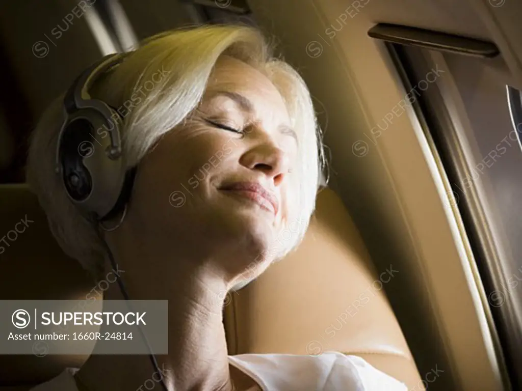 Close-up of senior woman wearing headphones and sleeping in an airplane